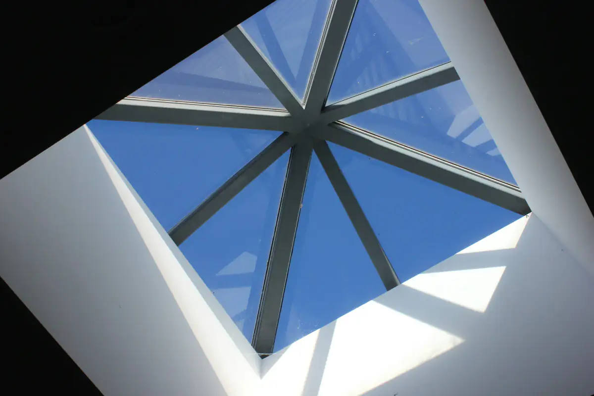 Pyramid roof lantern with slim white glazing bars framing a blue sky, viewed from the room below
