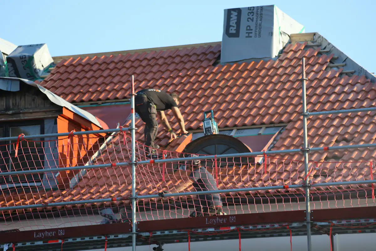 Roofer working on a clay tiled roof behind scaffolding with safety netting