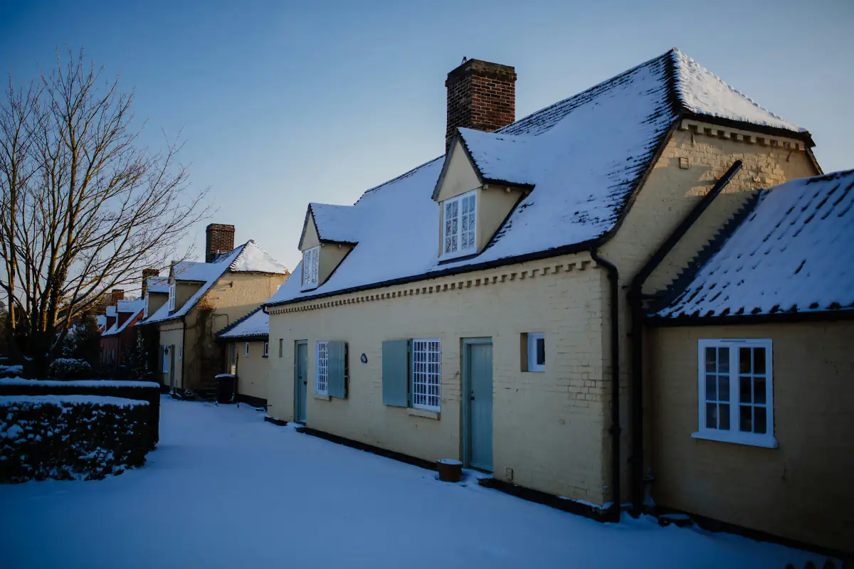 Snow on the tiled roofs of cream brick cottages at dusk in a Cambridgeshire village